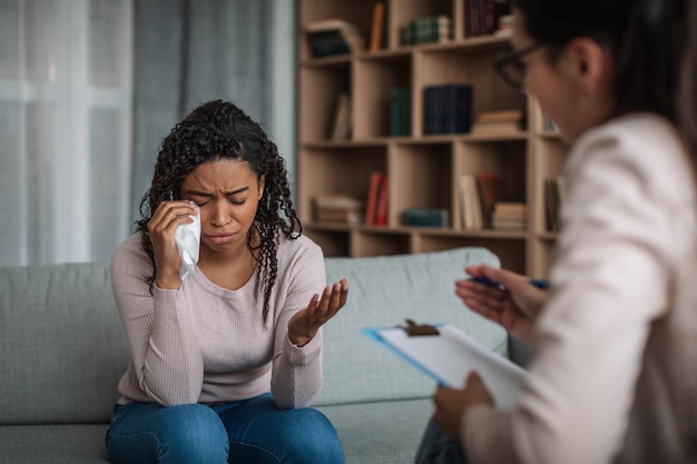 Depressed young black lady crying at consultation with european woman doctor psychologist with