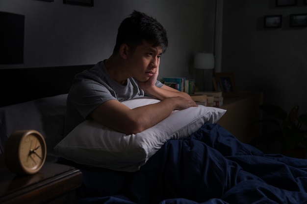 Depressed young man suffering from insomnia sitting in bed

