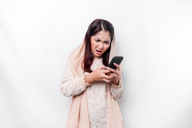 A depresses Asian Muslim woman wearing a headscarf looks stressed while talking on the phone isolated by white background