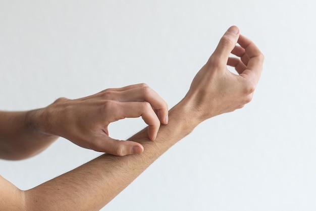 Dermatitis, eczema, allergy, psoriasis concept. man scratching itch on his arm, grey studio background. man itching rash on his elbow, copy space