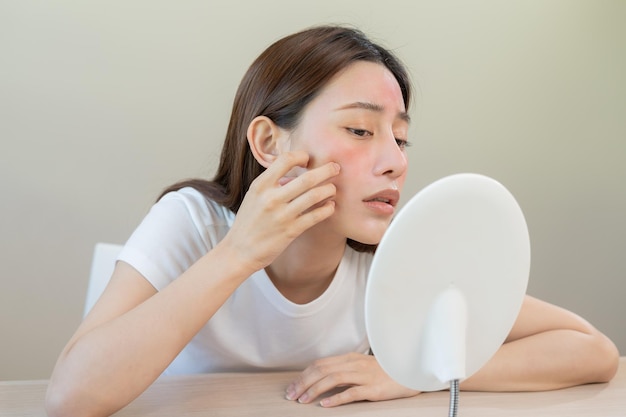 Dermatology puberty asian young woman girl looking into mirror allergy presenting an allergic reaction from cosmetic red spot or rash on face Beauty care from skin problem by medical treatment