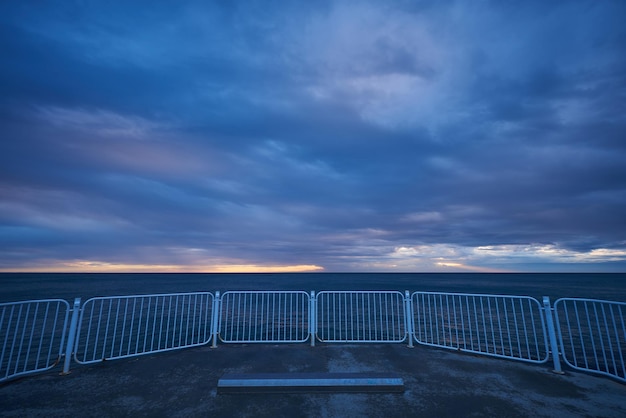 Deserted pier with dramatic sky over stormy dark sea at sunrise