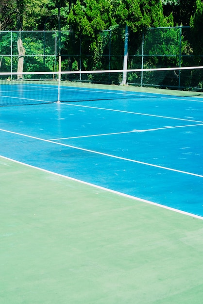 Deserted tennis court with greentrees in background in a public park on a sunny summer morning