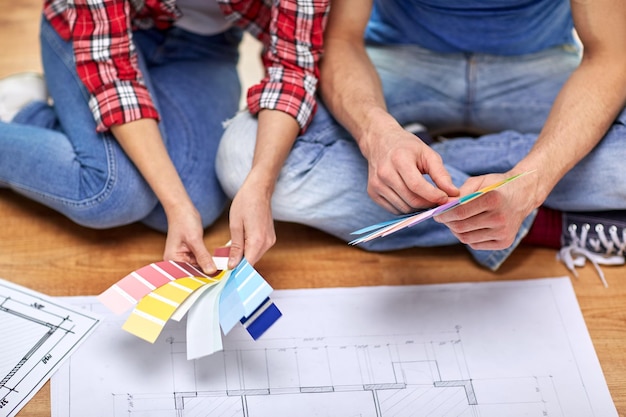 Photo design, repair, decoration and people concept - close up of couple with blueprint and color samples sitting on floor at home