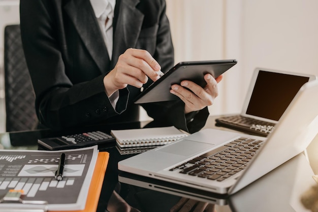 Designer using tablet with laptop and chart on desk in modern office.