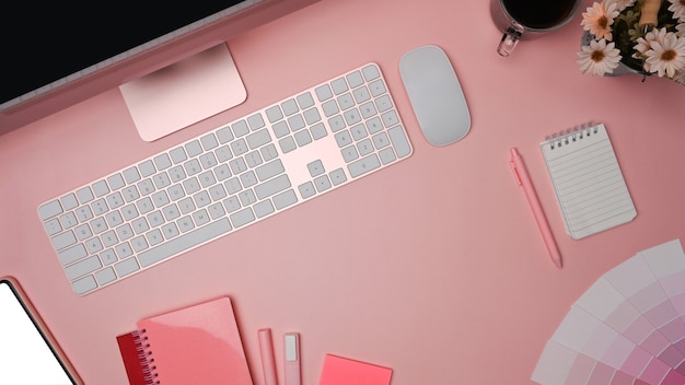 Designer workspace with computer, mobile phone and color swatches on pink background.