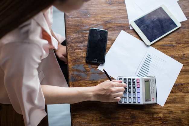 A desk for doing business with the hands of a young woman is calculating income and expenses.