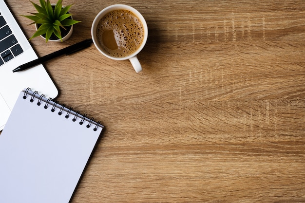 Desk office with laptop, blank notebook and coffee cup on wooden table