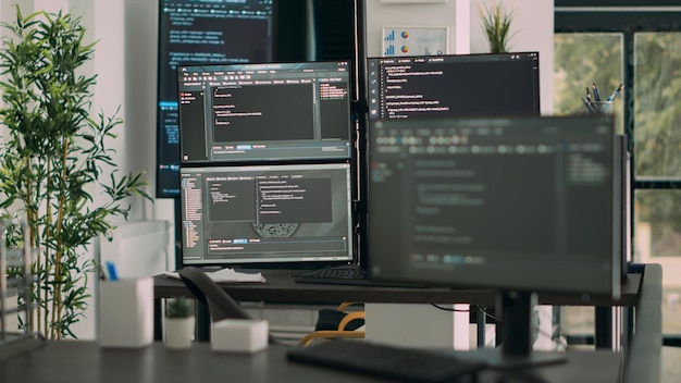 Desk with multiple screens showing digital programming network and artificial intelligence parsing code. Empty software developing company office with servers and database script.