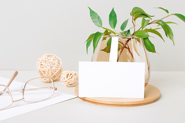 On the desktop are gold glasses, straw balls, green plant branches in a glass cup and a white blank card with a place to insert text. Home office. Close-up of the workplace. Business mockup