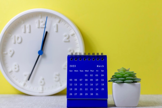 A desktop calendar for March 2023 and a clock on the table for planning your time