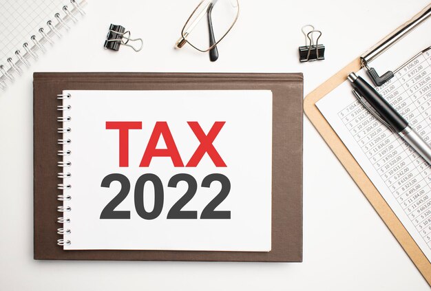 On the desktop there are reports, notepads, a calculator, a cash and a yellow sticker with the text TAX 2022. Business concept