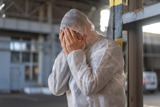 Despair healthcare worker in white covid protective overalls.Tired Male caucasian doctor grabs his head cower in depression during coronavirus pandemic Paramedic overworked cry covered face with hands