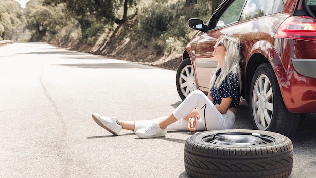 Despair woman sitting near the broken down car on road