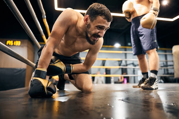 Desperate athlete staying on his knees before the opponent leaning on the floor with his right hand