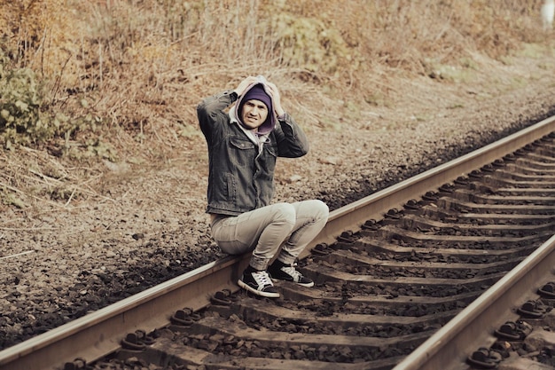 Desperate man sitting on railroad Side view of hopeless male in casual outfit touching head while sitting on rails in autumn countryside