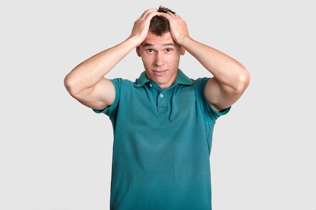 desperate young guy keeps both hands on head, regrets about something, wears casual outfit