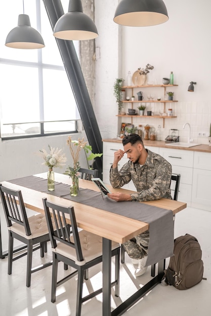 Despondent military man seated at the kitchen table holding the photo frame in his hand