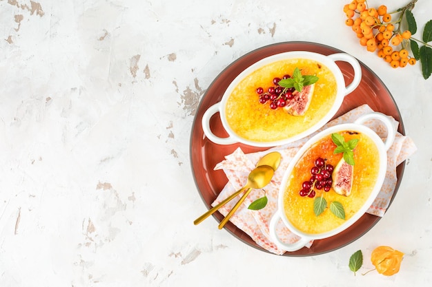 Dessert creme brulee with fresh figs and currants and mint leaves in white bowls on a light stone background in an autumn composition Delicious dessert for two Top view