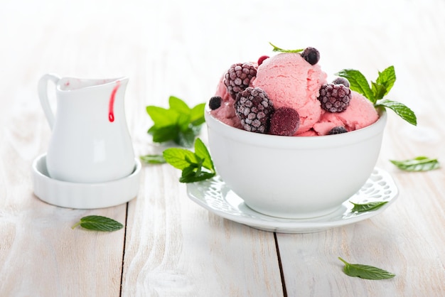 Photo dessert of ice cream made from berries served with mint and sauce on a light wooden surface selective focus