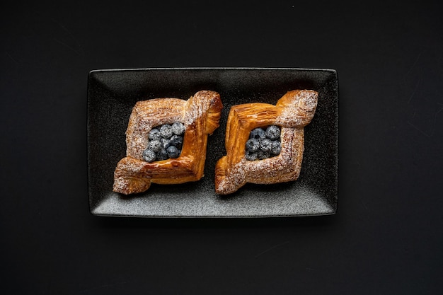 Dessert is a small puff pastry pie with stuffing inside on a black serving plate on a black background A piece of cake with a cut