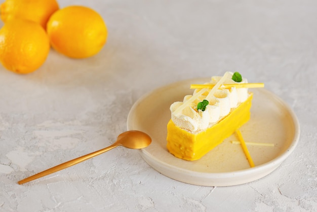 Dessert lemon cake with whipped cream and yellow chocolate with spoon on a light table