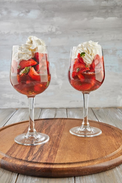 Dessert of strawberries and whipped cream in tall glasses on wooden background