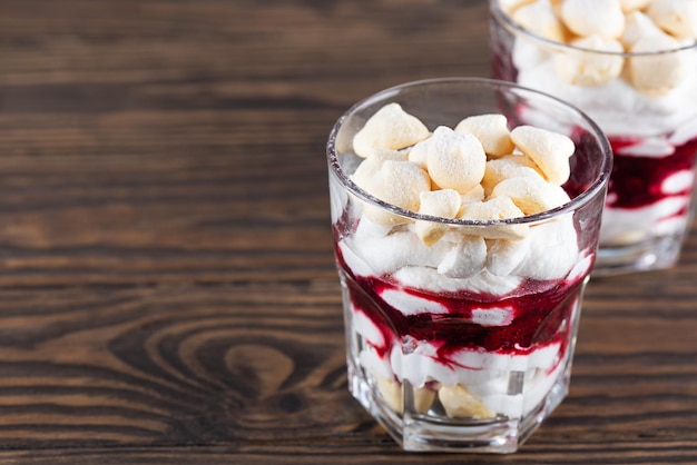 Dessert with aquafaba meringue coconut cream and cherries in a glass on a wooden table