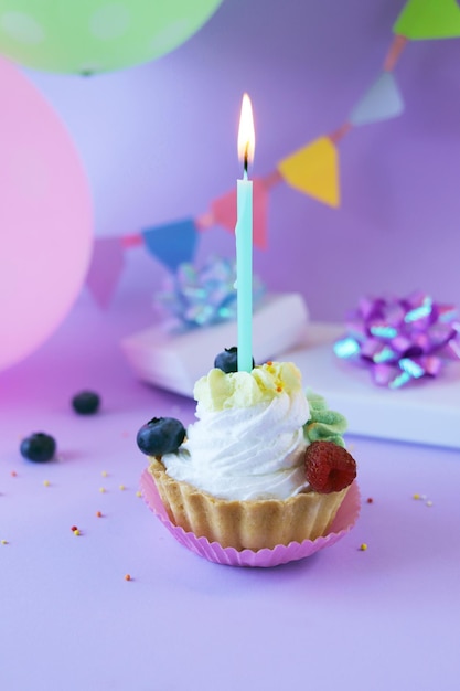 Dessert with white cream decorated with fresh berries and burning candles, lilac background