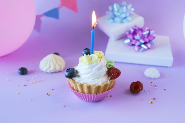 Dessert with white cream decorated with fresh berries and burning candles, lilac background