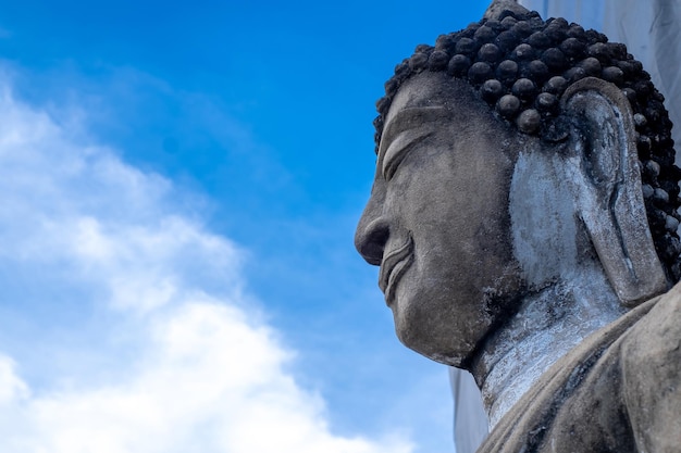 Detail of the face of a representation of the buddha with his eyes closed on blue nature sky background the from under view