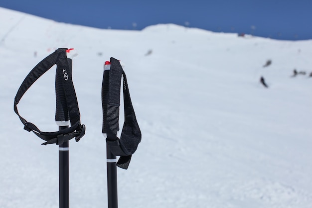 Photo detail on ski poles hand grip, with blurred piste with skiers and deep blue sky in background.