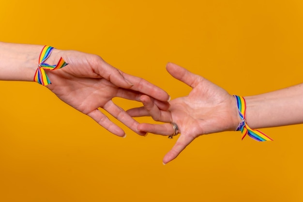 Detail of two hands of two women caressing and touching each other's fingers LGBT concept on a yellow background couple of lesbian girls