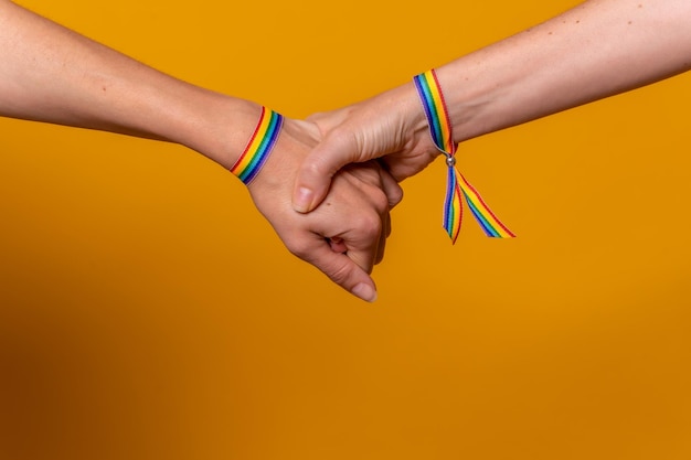 Detail of two hands of two women shaking hands with a bracelet LGBT concept on a yellow background couple of lesbian girls