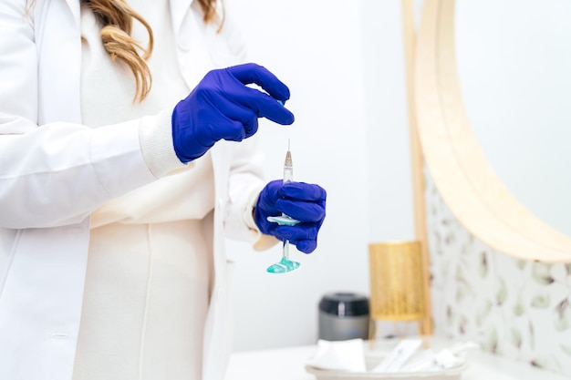 Detail of unrecognizable clinicians hands with blue gloves holding a syringe for hyaluronic acid application in cosmetic clinic