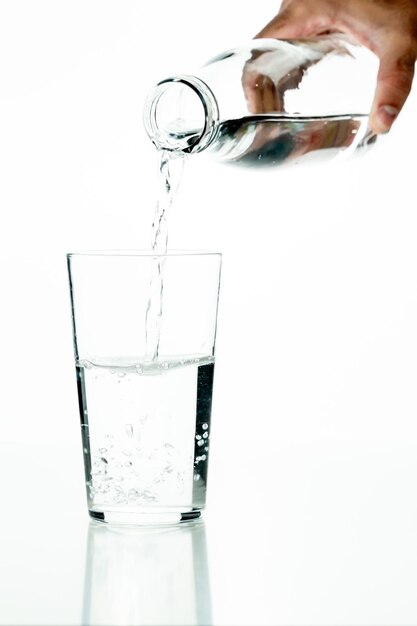 Detail of an unrecognizable man39s hand pouring water into a crystal glass on a white background