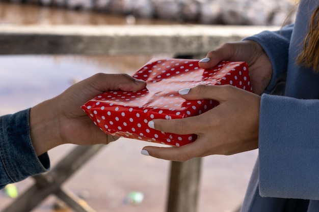 Detail of a woman's hands handing a gift on Valentine's Day and a man's hands picking up the gift