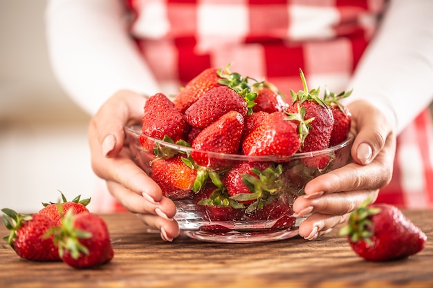 Detail of woman's hands holding a bowl full of fresh strawberries on a table.