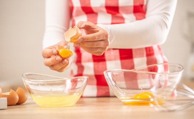 Detail of woman's hands separating egg yolks from the whites into two glass bowls.