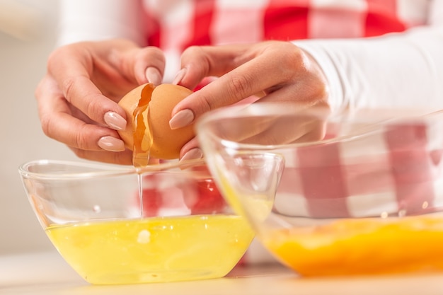 Detail of woman's hands separating egg yolks from the whites into two glass bowls.