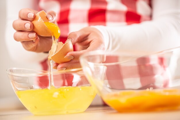 Detail of woman's hands separating egg yolks from the whites into two glass bowls.