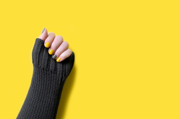 Detail of womans hand wearing gray sweater with trendy colors illuminating yellow and ultimate grey manicure nails