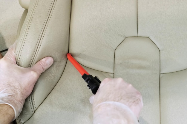 Detailing of the interior of a modern car A man inflates the wrinkles on a beige car seat with a compressor Car cleaning specialist View from above