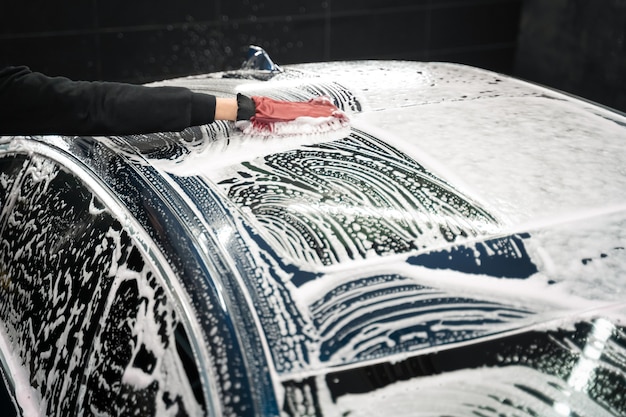 Detailing worker washes the vehicle body with foam and rag