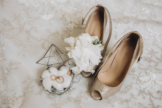 details of the brides clothes gold wedding rings in a glass decorative box standing on cotton flowers Wedding flower of the groom Womens highheeled shoes of golden color