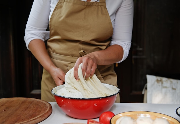 Details chef's hands kneading raising yeast dough in a vintage enamel red bowl while preparing bread in rustic kitchen