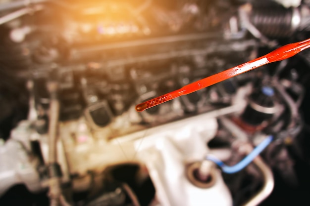 Deteriorating car oil on dipstick with background of blurred engine compartment automotive maintenance business concept