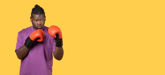 Determined african sportsman posing with boxing gloves over yellow background