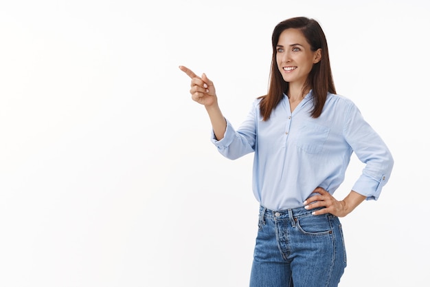 Determined businesswoman feel motivated win deal, achieve success, stand half-turned pointing looking pleased left copyspace, see good deal, business concept, stand confident white wall