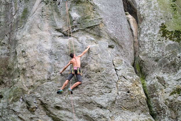 Determined climber clambering up steep wall of rocky mountain. Sportsman overcoming difficult route. Engaging in extreme sports and rock climbing hobby concept.